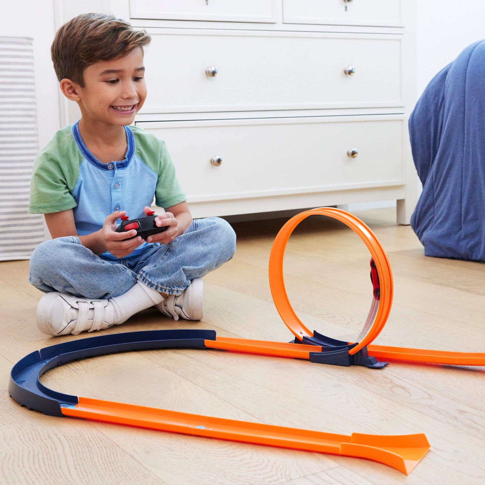 Berniukas pulteliu vairuoja Ferrari per oranžinės Hot Wheels trasos kilpą