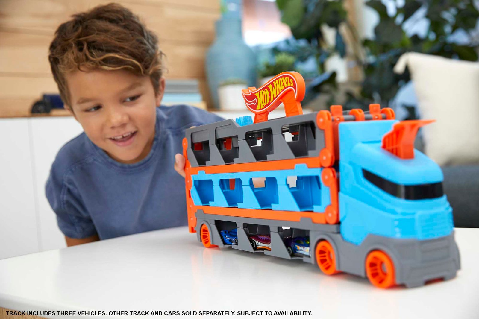 Berniukas žaidžia su mėlynu Hot Wheels City transporteriu ant stalo