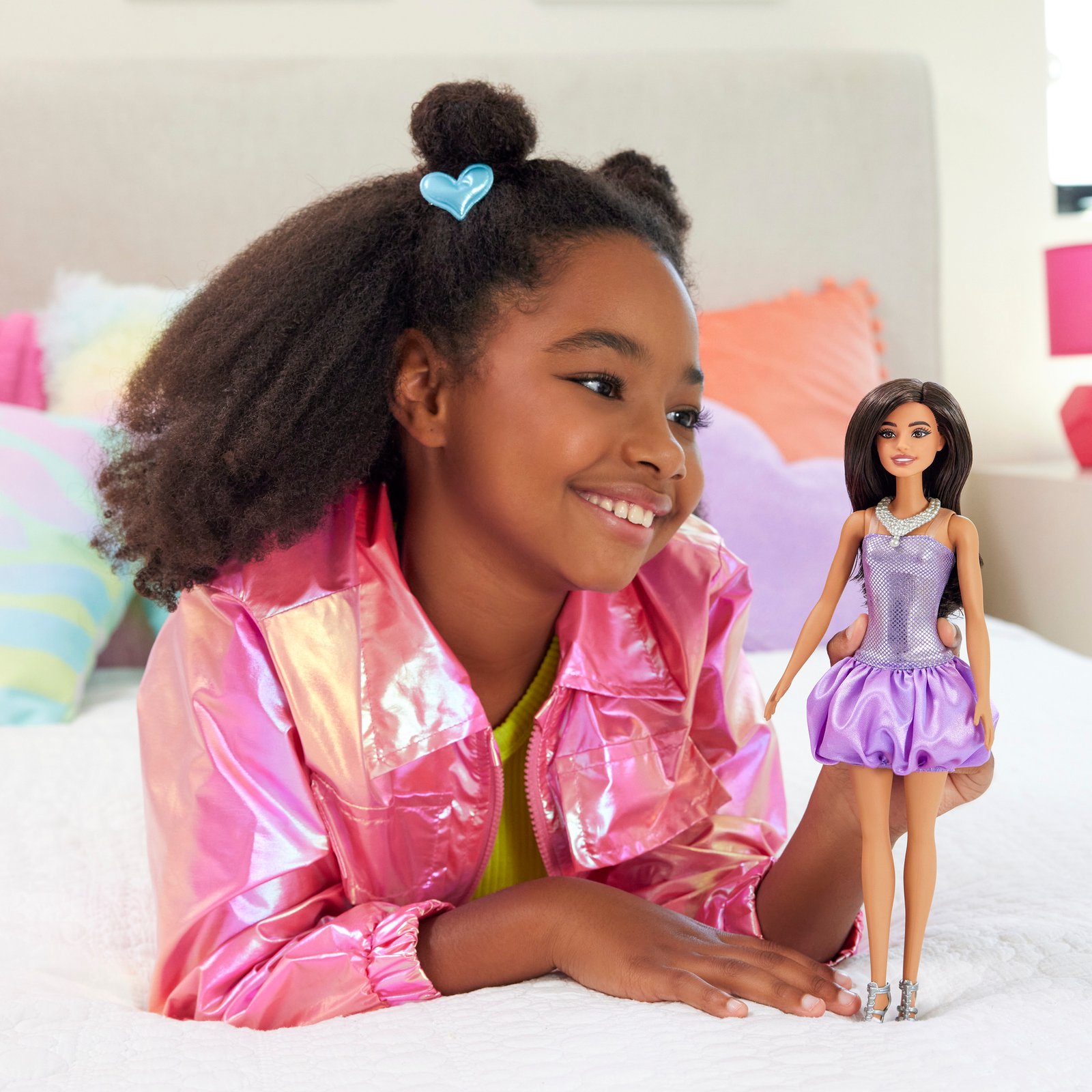 Mergaitė ant lovos šalia rudaplaukės Barbie lėlės pūsta suknele