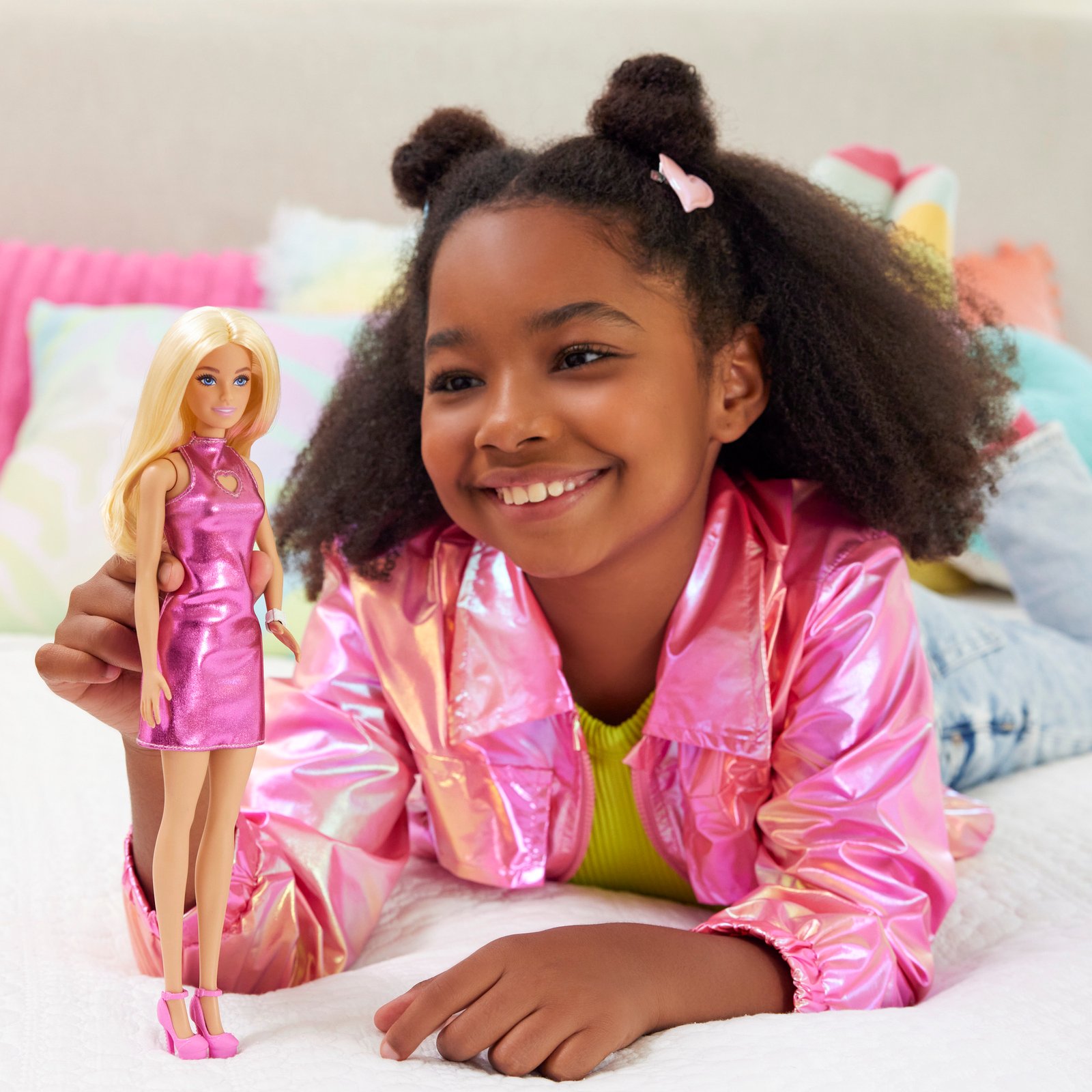 Mergaitė guli ant lovos ir laiko Barbie madistę rožine suknele