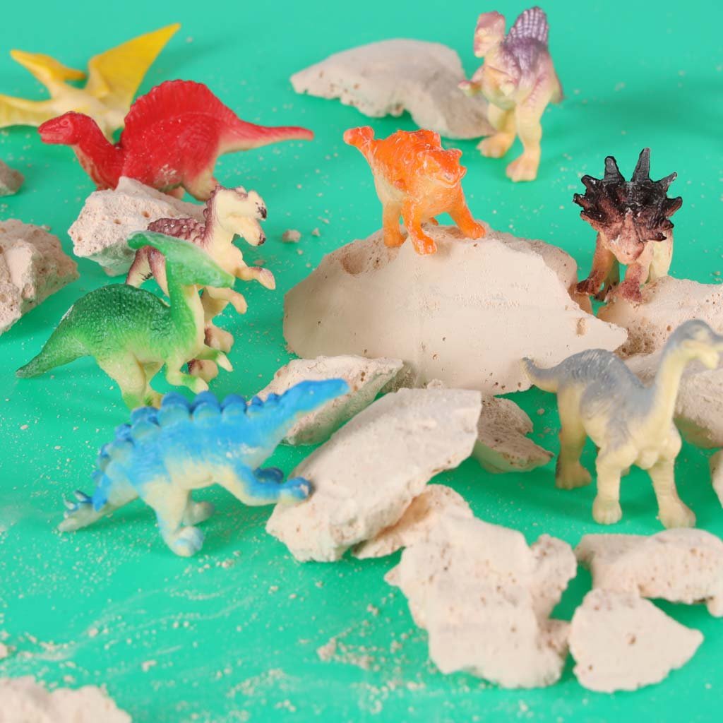 Dinozaurų figūrėlės prie suskaldyto kiaušinio likučių