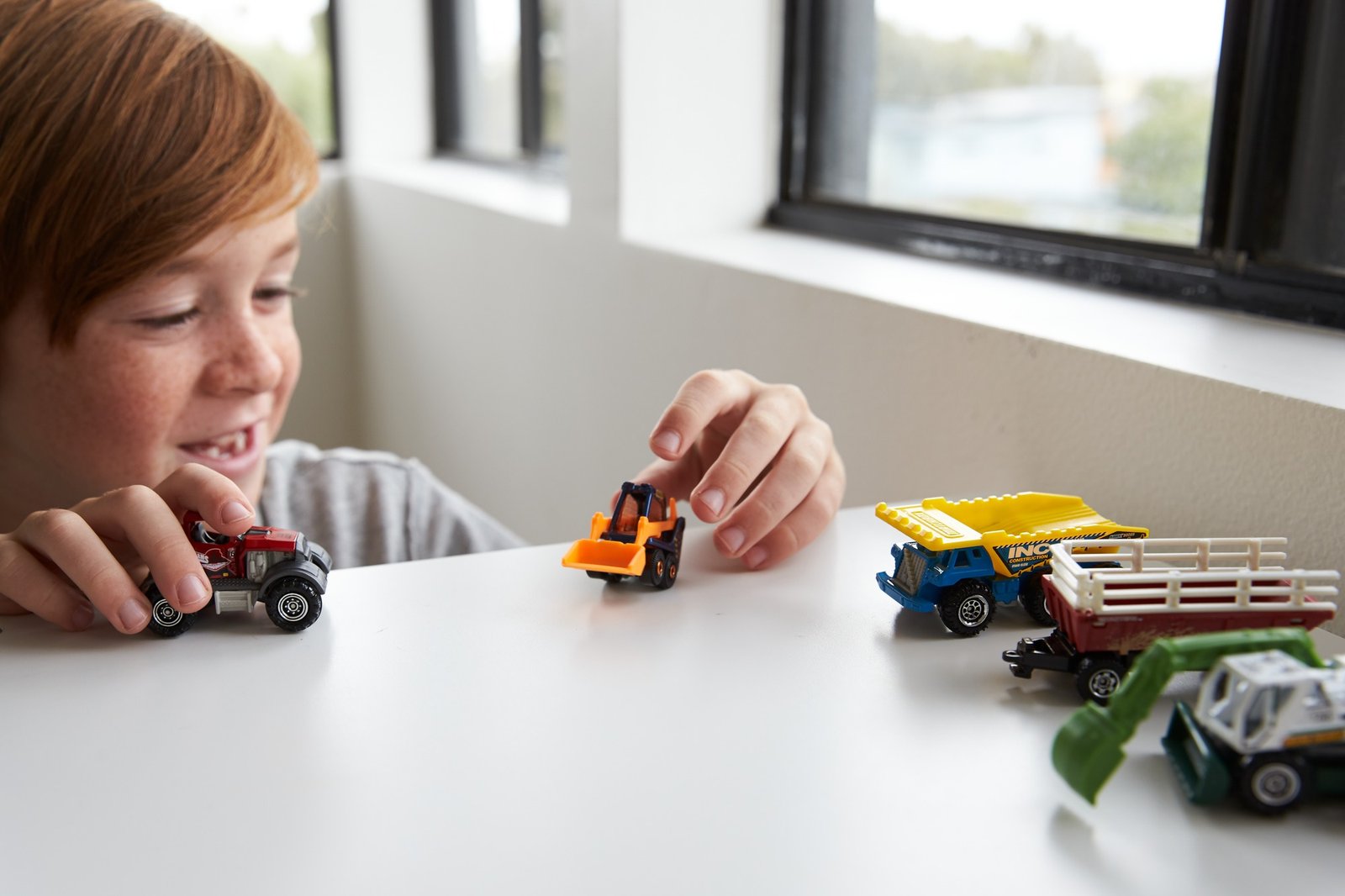 Berniukas žaidžia su Matchbox mašinėlėmis prie stalo